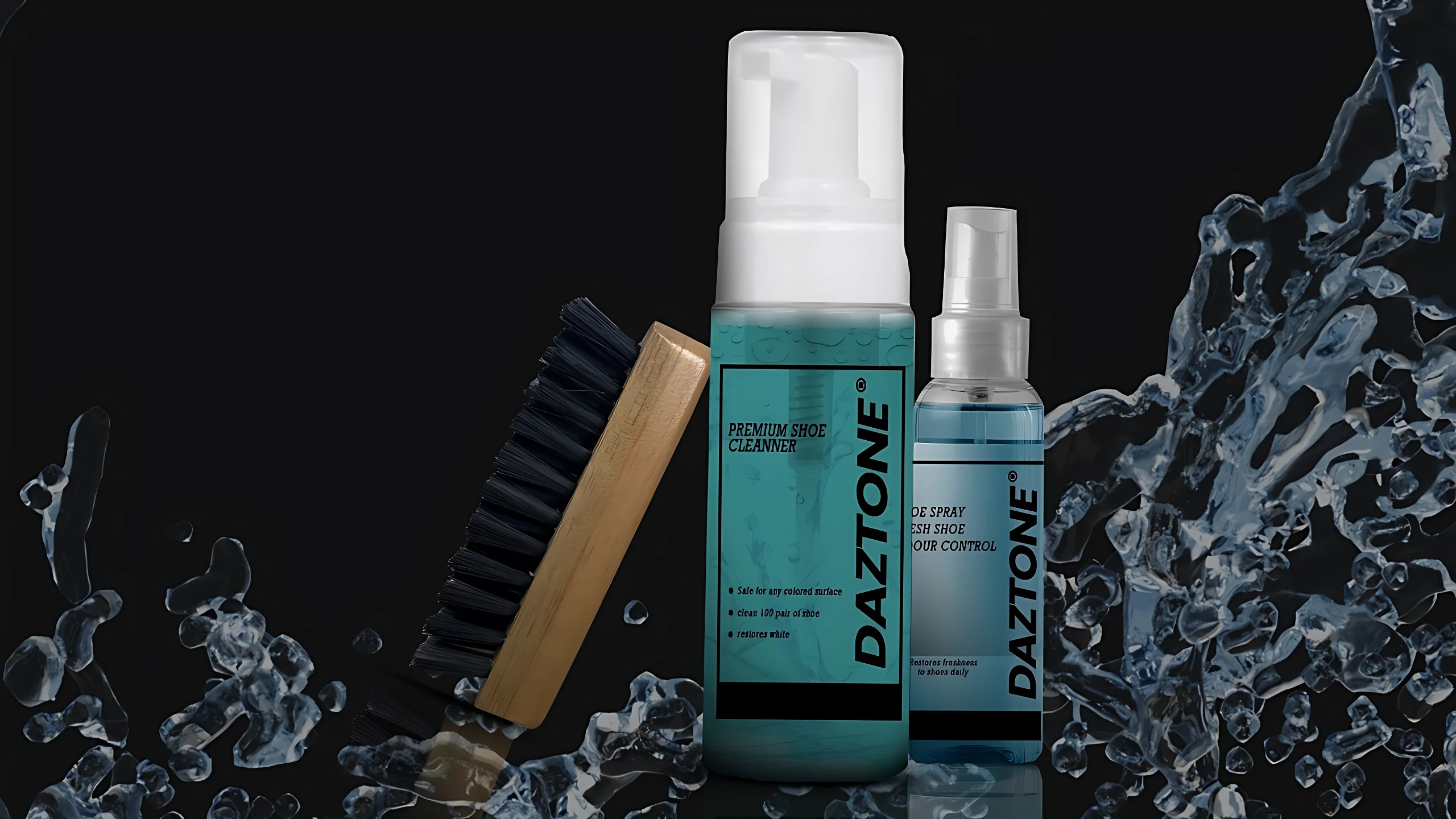 Kit de limpieza Daztone para calzado: cepillo de cerdas negras con mango madera, spray azul translúcido y botella de espuma azul con tapa blanca, sobre fondo negro con salpicaduras de agua.