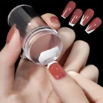 Mano con uñas esmaltadas en tono rosado con tipografía francesa blanca, aplicando polvo blanco desde un frasco transparente sobre la uña índice; fondo negro con cuatro uñas adicionales mostrando el diseño final.