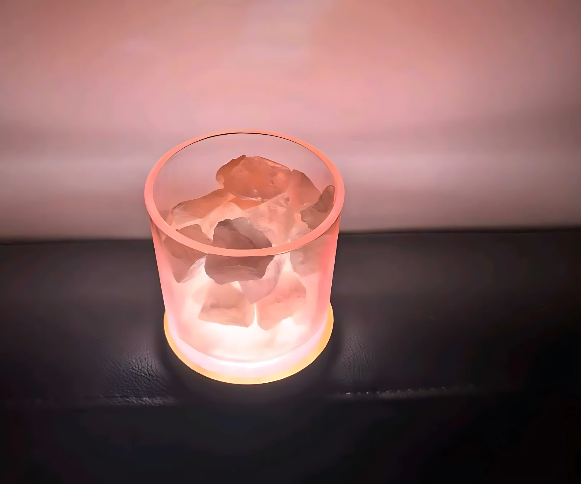 Lámpara aromatizante con cristales de sal natural y base luminosa rosada, sobre superficie oscura.