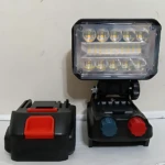 Lámpara de trabajo inalámbrica con batería incluida, panel LED frontal y controles rotativos en base negra.