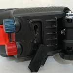 Lámpara de trabajo inalámbrica negra con panel lateral USB, perillas azul y roja, y soporte ajustable para montaje.