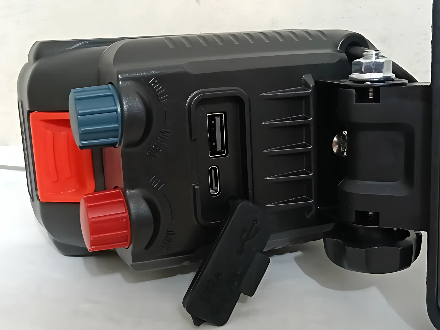 Lámpara de trabajo inalámbrica negra con panel lateral USB, perillas azul y roja, y soporte ajustable para montaje.