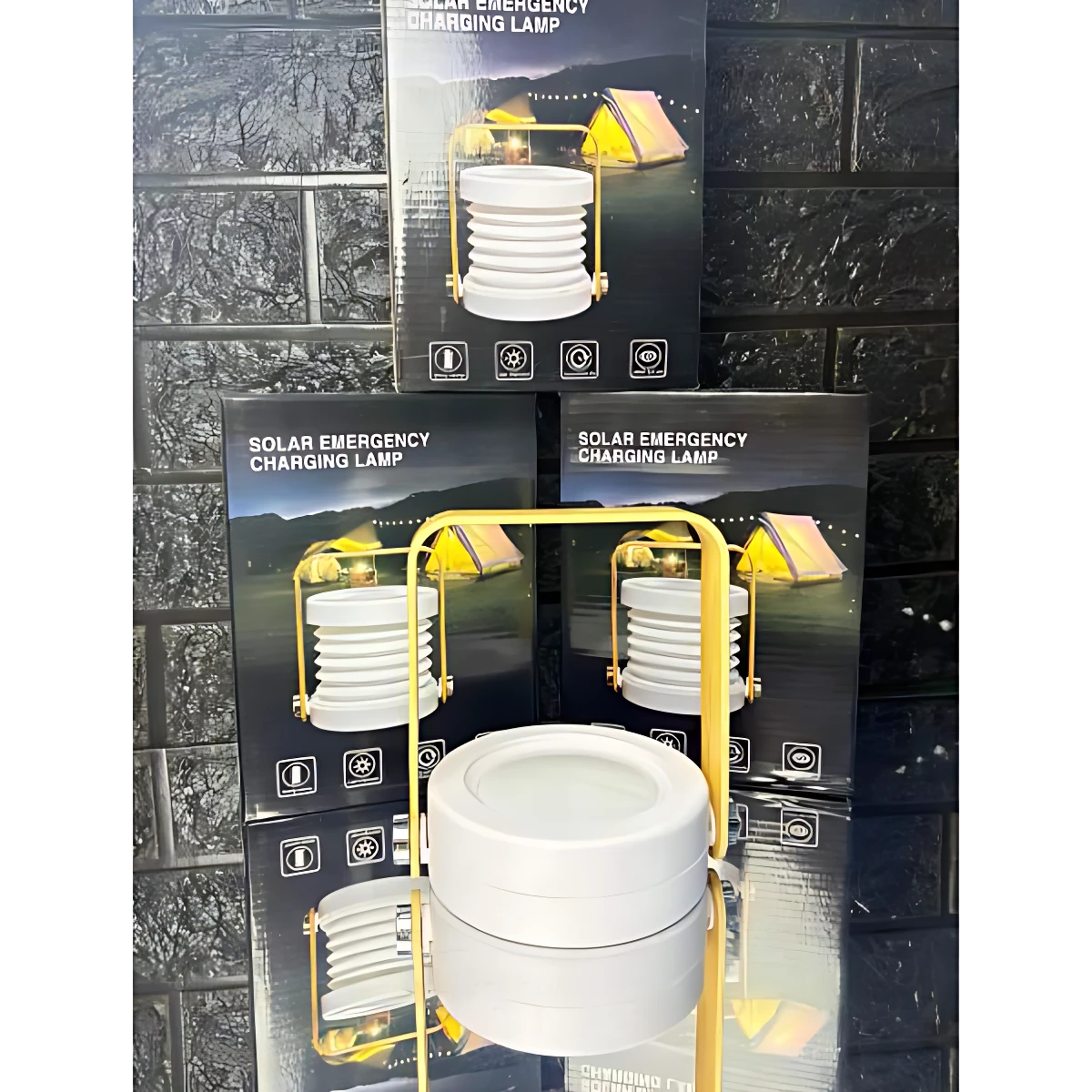 Lámpara plegable solar blanca con marco amarillo, montada sobre su caja de venta al por mayor, mostrando diseño compacto y funcional para emergencias.