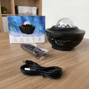 Lámpara proyector galaxia LED negra con control remoto y cable USB, junto a su caja de presentación.