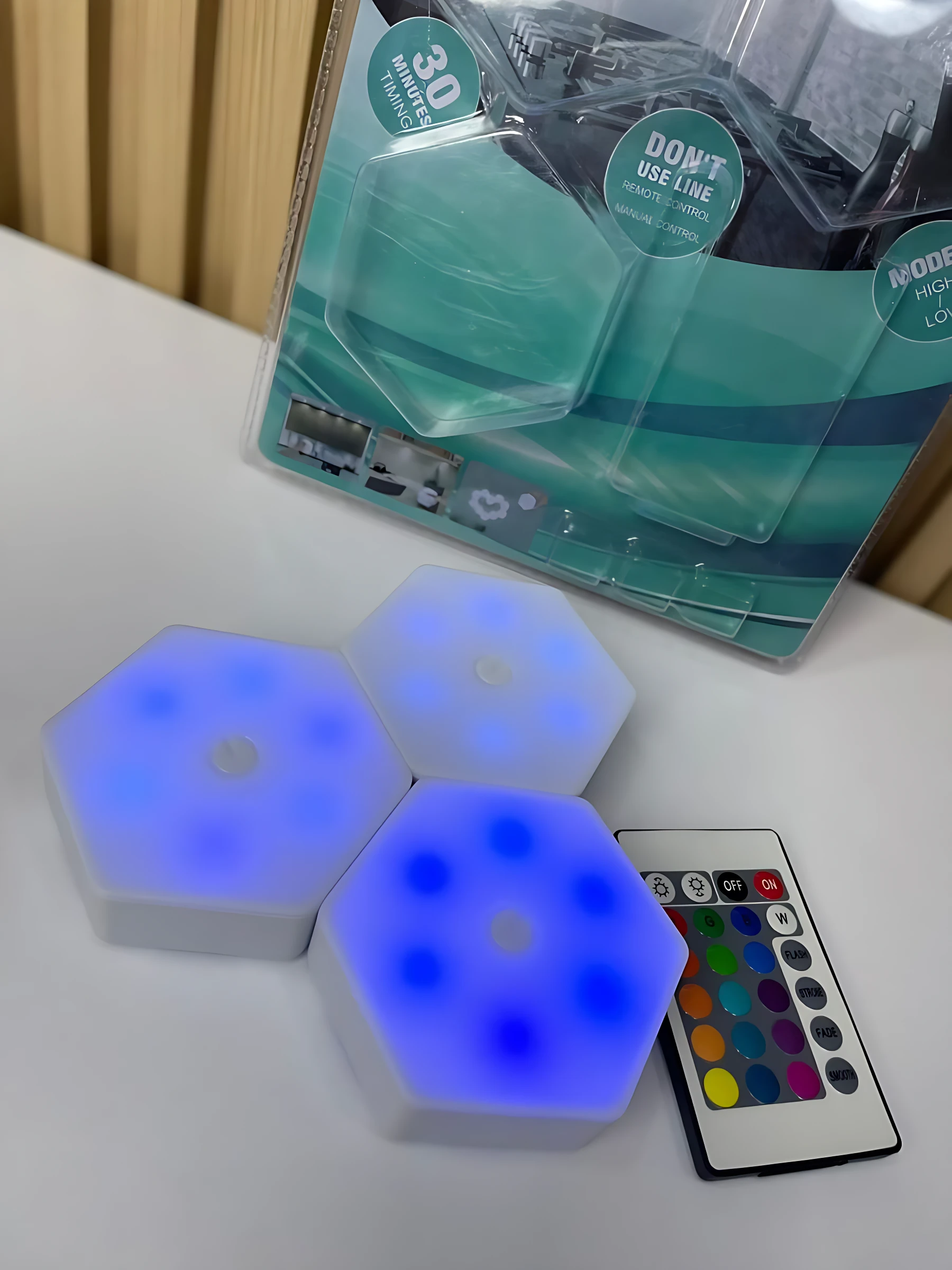 Tres lámparas LED hexagonales en azul brillante, con control remoto multicolor y empaque original visible en el fondo.