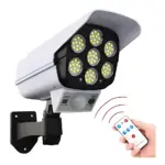 Cámara solar blanca con seis luces LED amarillas, sensor de movimiento y mando a distancia, montada en pared para disuadir intrusos.