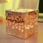 Lámpara de mesa con efecto espejo infinito, tulipanes en luz cálida, diseño cúbico transparente con detalles en plástico translúcido.