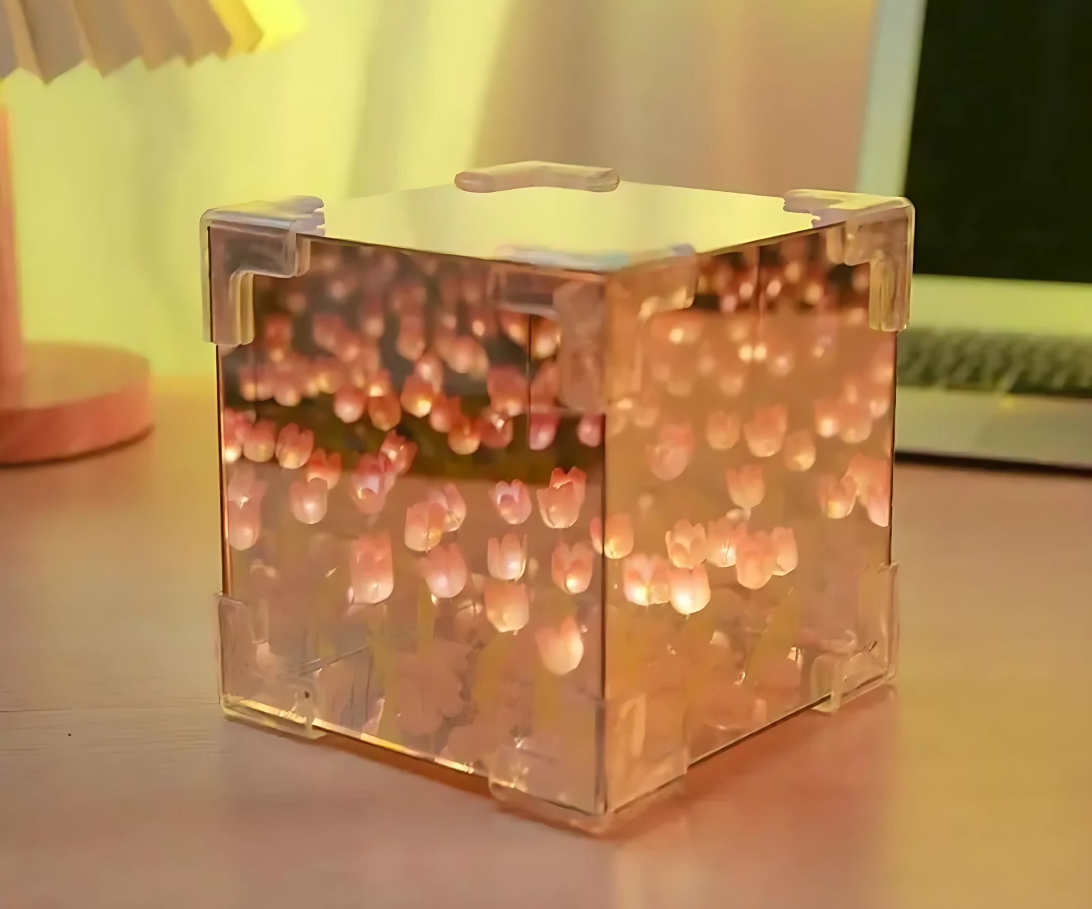 Lámpara de mesa con efecto espejo infinito, tulipanes en luz cálida, diseño cúbico transparente con detalles en plástico translúcido.