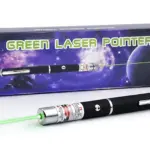 Láser pointer verde con carcasa negra y detalles plateados, emitiendo rayo láser visible. Incluye caja con diseño espacial y texto en inglés.