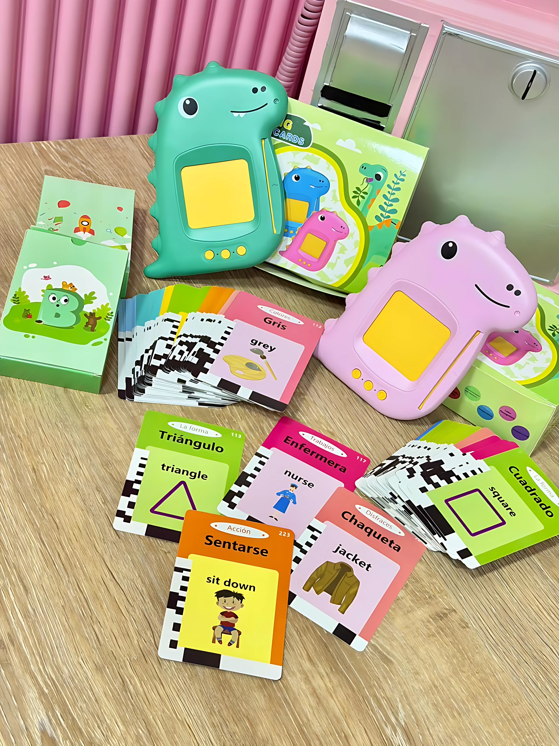 Lector de inglés interactivo para niños en colores verde y rosa, con tarjetas de vocabulario en español e inglés sobre mesa de madera.