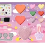 Paleta de maquillaje infantil con cosméticos lavables, incluye brochas, labiales, sombras y accesorios en tonos pastel sobre fondo rosa.