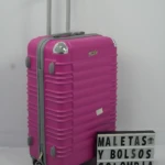 Maleta rígida rosa con ruedas giratorias y asa telescópica, junto a letrero que dice MALETAS Y BOLSOS COLOMBIA.