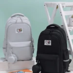 Mochila escolar Jiaheng en gris claro y negro, con diseño compacto, bolsillo frontal y soporte para audífonos. Ideal para portátiles de 15.6 pulgadas.