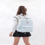 Mochila escolar Jiaheng en color azul claro, vista posterior con mochila de gran capacidad para portátil 15.6 pulgadas, usada por estudiante con uniforme.