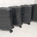 Cuatro maletas Ultra Flex 22 de polipropileno negro, con ruedas giratorias y diseño rígido, dispuestas en fila sobre piso blanco.