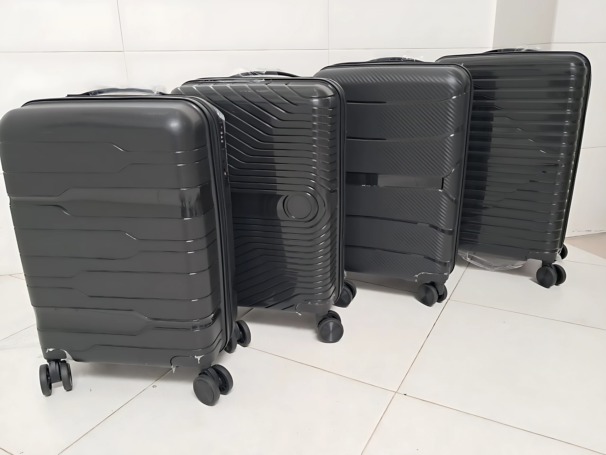 Cuatro maletas Ultra Flex 22 de polipropileno negro, con ruedas giratorias y diseño rígido, dispuestas en fila sobre piso blanco.