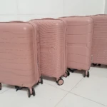 Cuatro maletas Ultra Flex 22 en tono rosa pálido, con diseño de líneas horizontales y ruedas giratorias, dispuestas en fila sobre piso blanco.