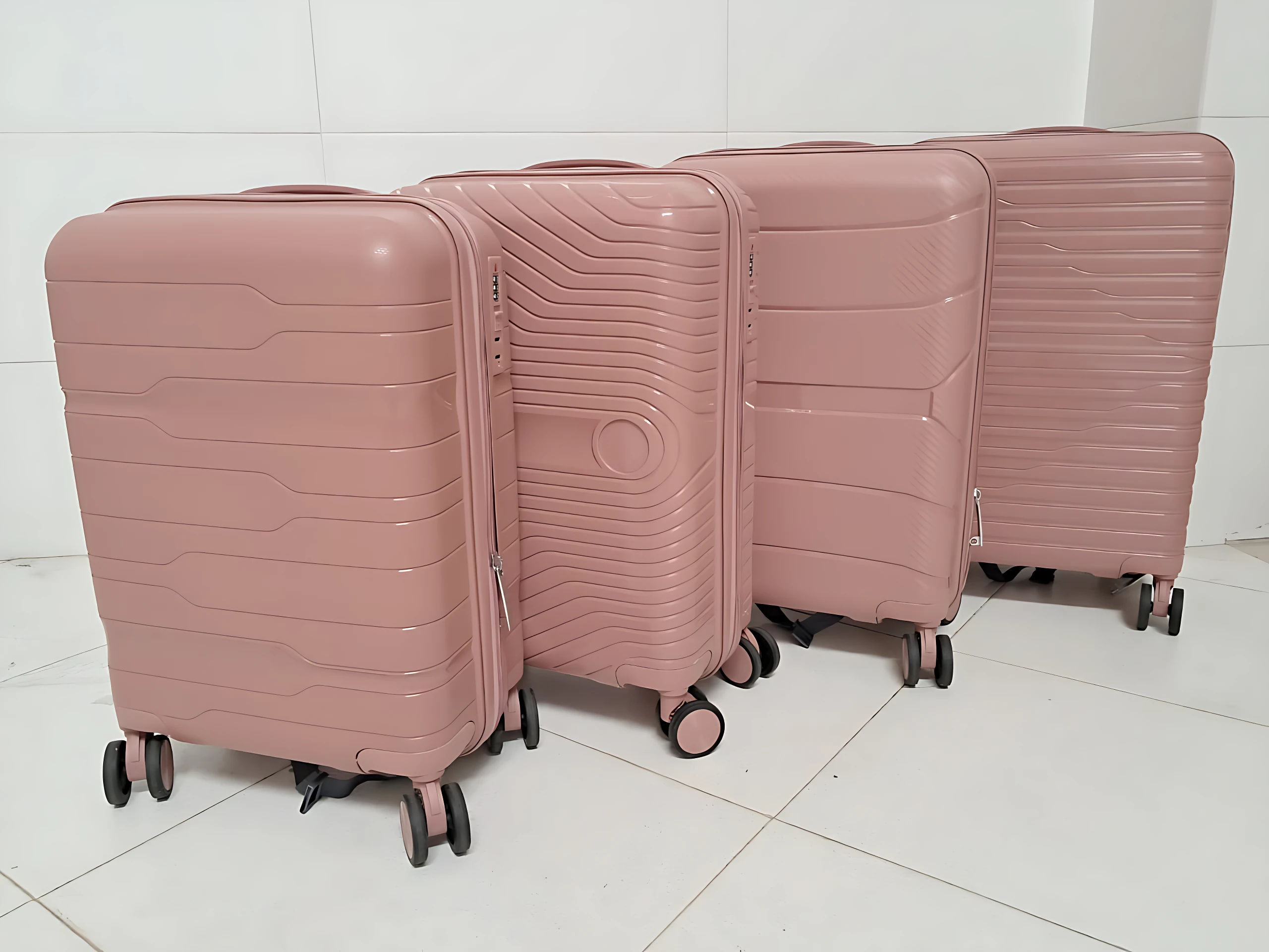 Cuatro maletas Ultra Flex 22 en tono rosa pálido, con diseño de líneas horizontales y ruedas giratorias, dispuestas en fila sobre piso blanco.