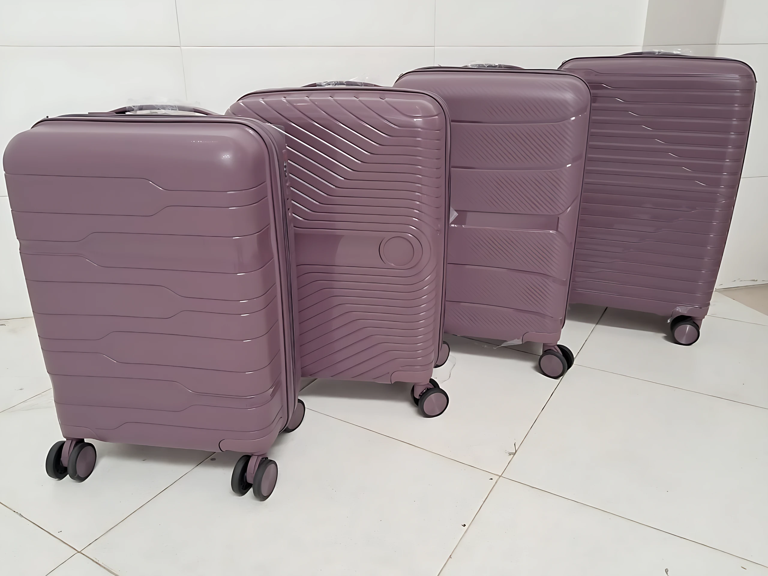 Cuatro maletas Ultra Flex 22 en tono lila, de polipropileno resistente, con ruedas giratorias y diseño estructurado, dispuestas en fila sobre suelo blanco.