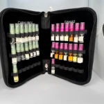 Maletín negro acolchado abierto, mostrando organizadores para muestras de perfumes. Lado izquierdo con frascos verdes etiquetados como Caballeros, lado derecho con frascos rosas y amarillos etiquetados como Damas.