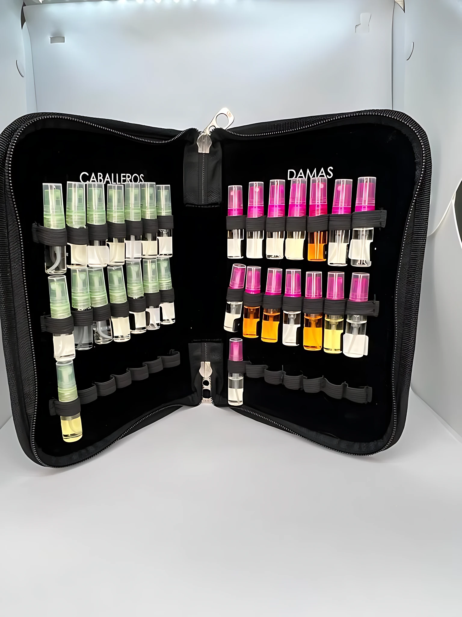 Maletín negro acolchado abierto, mostrando organizadores para muestras de perfumes: sección Caballeros con frascos verdes y Damas con frascos rosas y amarillos, ambos con tapones de colores.