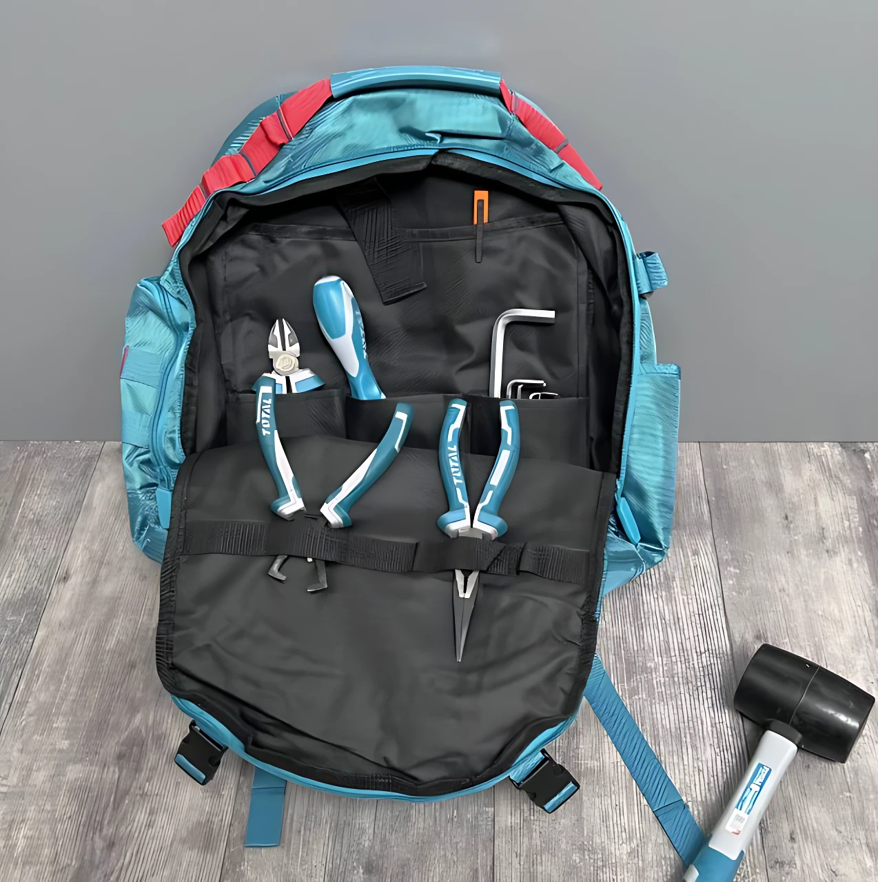 Mochila industrial azul con herramientas organizadas en compartimentos internos, incluyendo alicates, destornilladores y llave hexagonal, sobre superficie de madera.