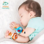 Bebé durmiendo con dos manillas didácticas en forma de pez, una azul y otra naranja, sobre fondo blanco suave.