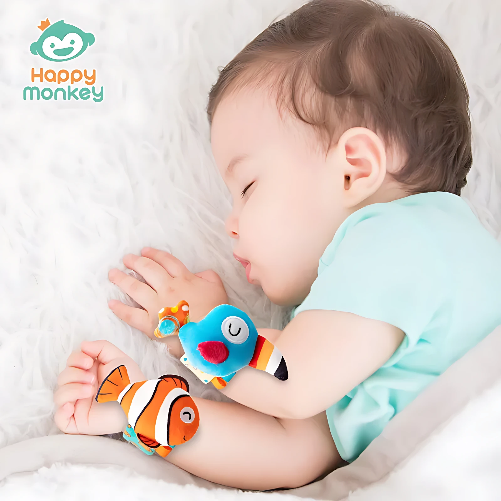 Bebé durmiendo con dos manillas didácticas en forma de pez, una azul y otra naranja, sobre fondo blanco suave.