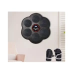 Máquina de boxeo musical con seis colchonetas negras en forma de flor, montada en pared blanca, junto a guantes de entrenamiento negros con detalles blancos.