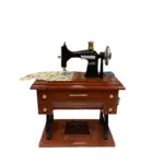 Caja de música mecánica con maquina de coser vintage en madera oscura, con detalles dorados y tela estampada sobre la superficie.