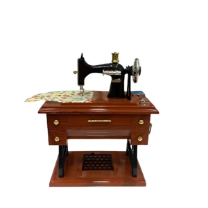 Caja de música mecánica con maquina de coser vintage en madera oscura, con detalles dorados y tela estampada sobre la superficie.