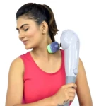 Mujer usando masajeador eléctrico blanco con cabezal verde y morado en cuello, mostrando uso práctico para alivio muscular.