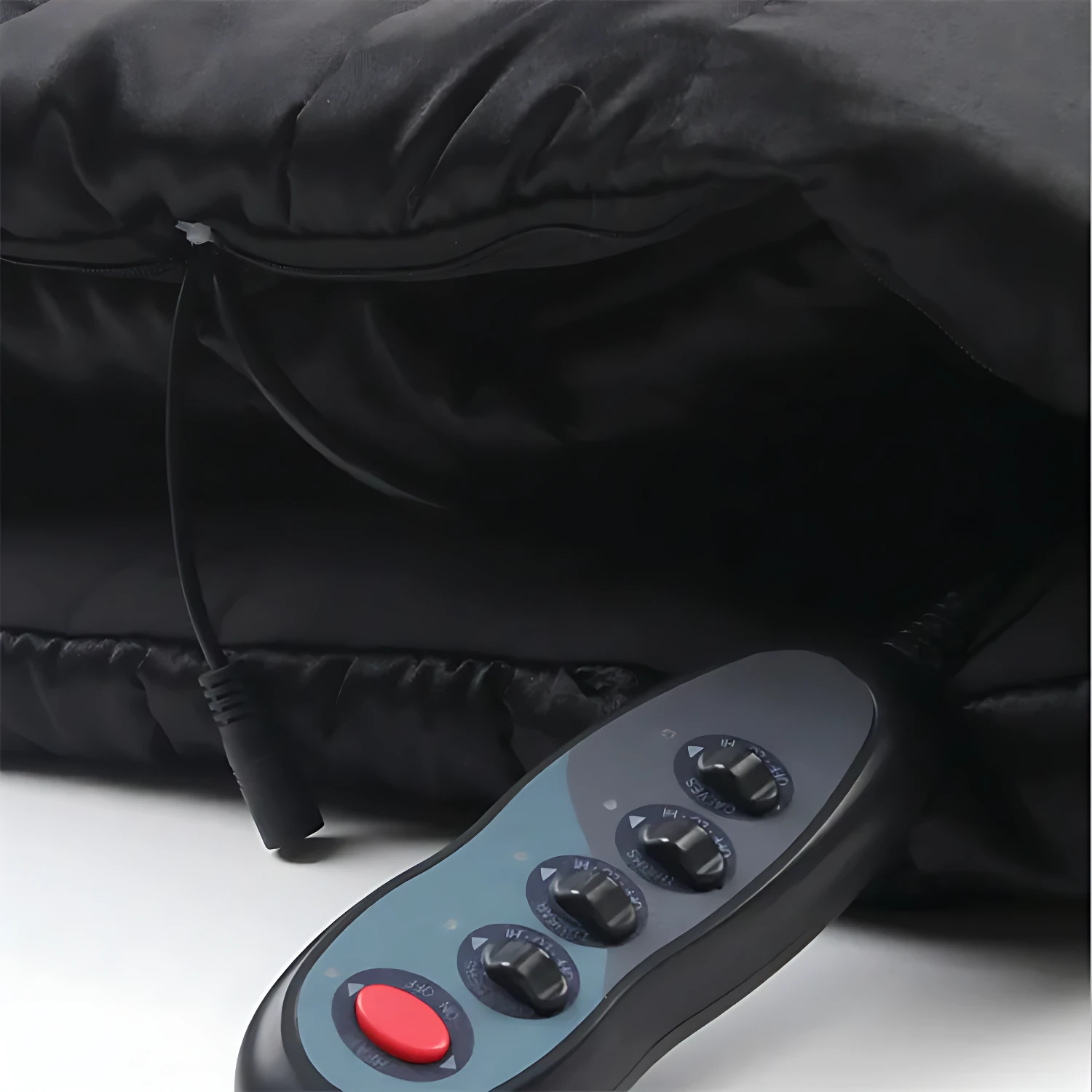 Control remoto negro con botones de ajuste y botón rojo, junto a colchoneta negra plegable con cable conectado.