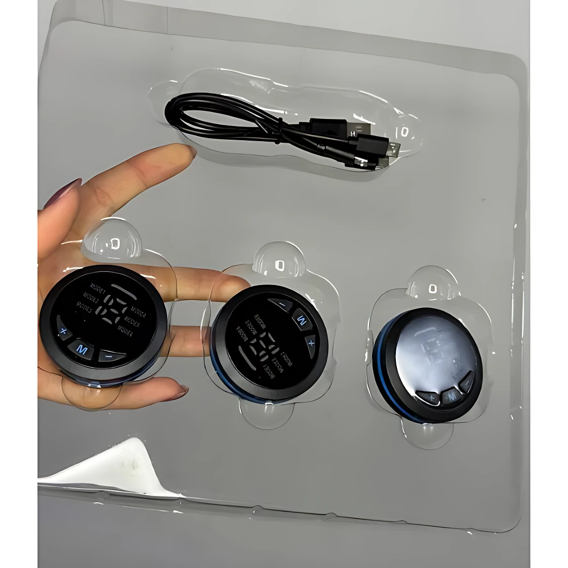 Pack de masajeador escultor EMS con tres unidades negras, cable USB y base transparente.