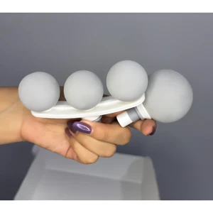 Masajeador percutor portátil blanco con cuatro cabezales esféricos de goma, sostenido en mano para mostrar su tamaño y diseño ergonómico.