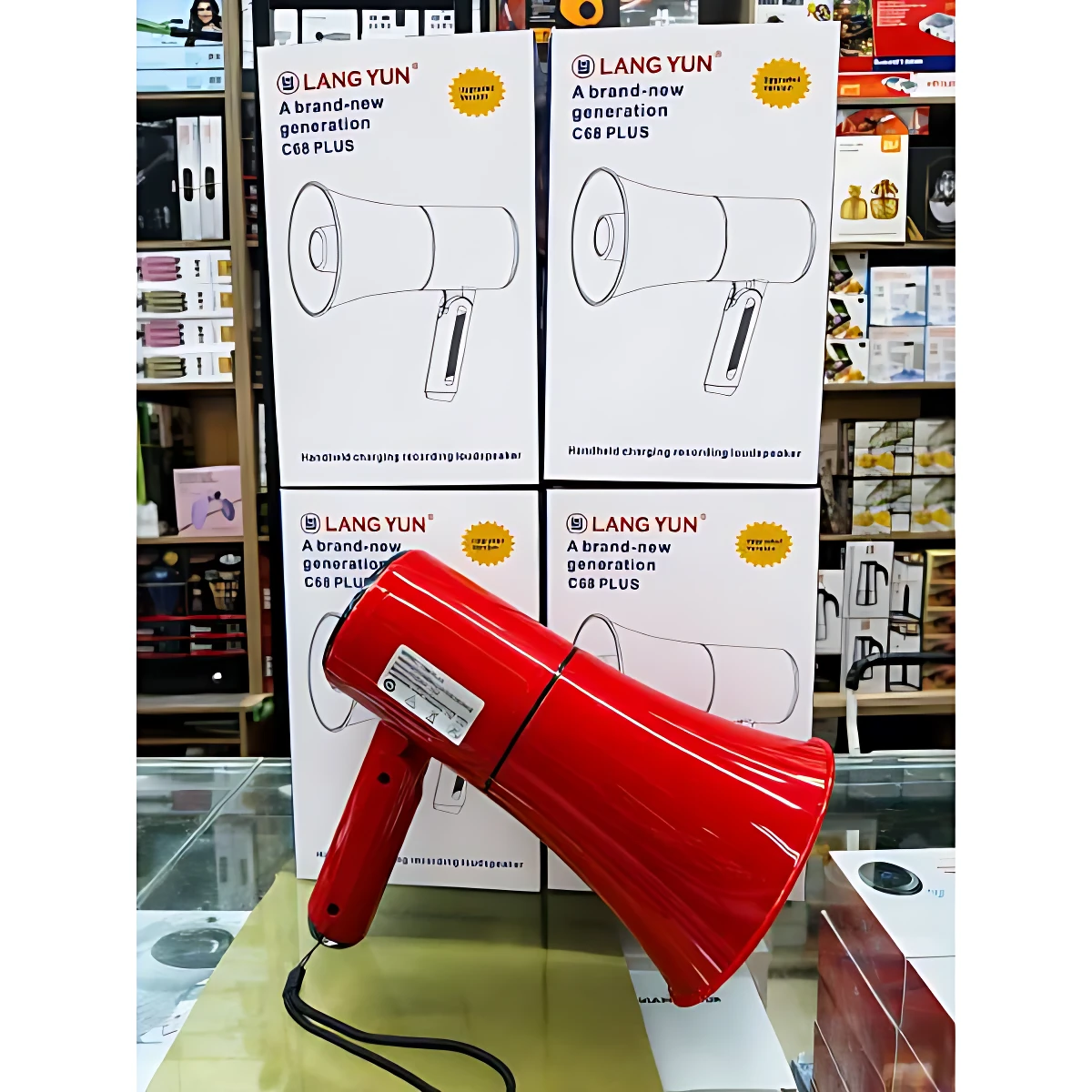 Megáfono Lang Yun C68 Plus en color rojo brillante, con cable negro visible, sobre mostrador de vidrio; caja blanca con del producto y texto en español al fondo.