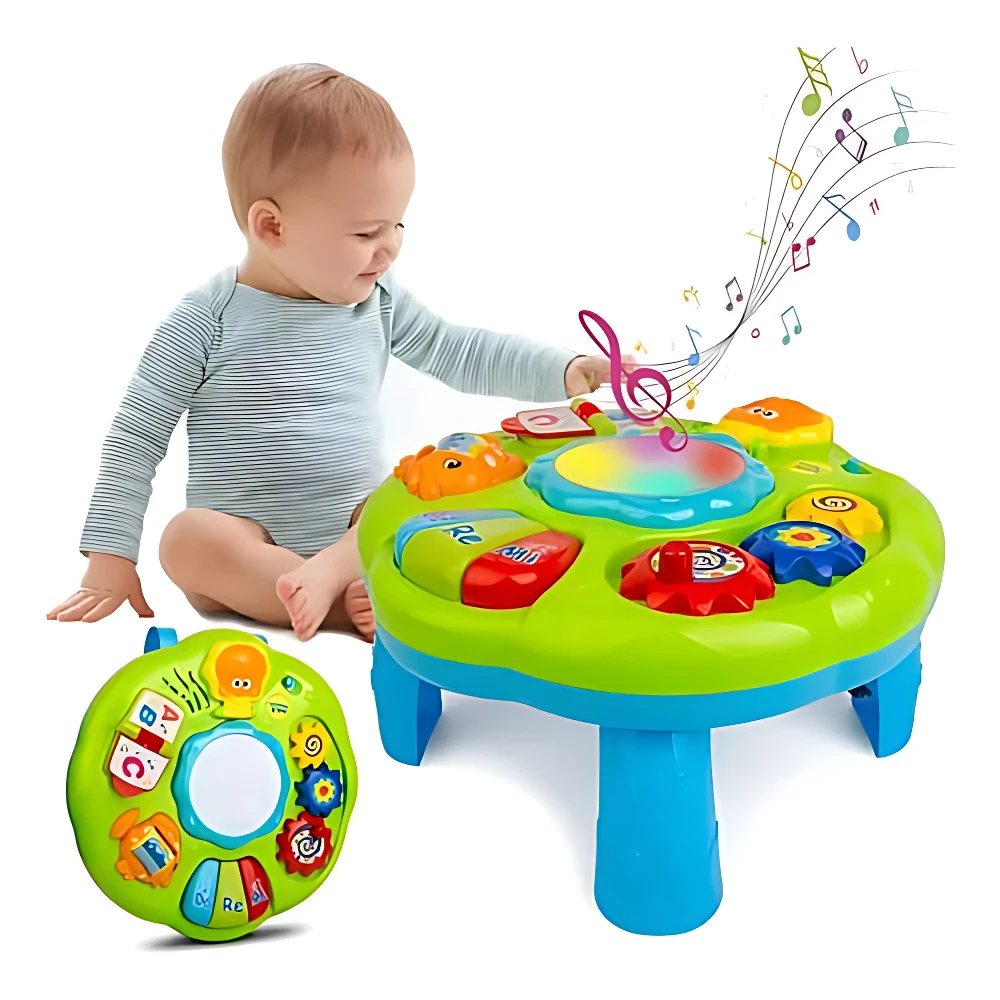 Mesa didáctica sensorial verde con piano, espejos y botones de colores; bebé interactúa con ella. Incluye panel circular adicional con teclas musicales y formas geométricas.