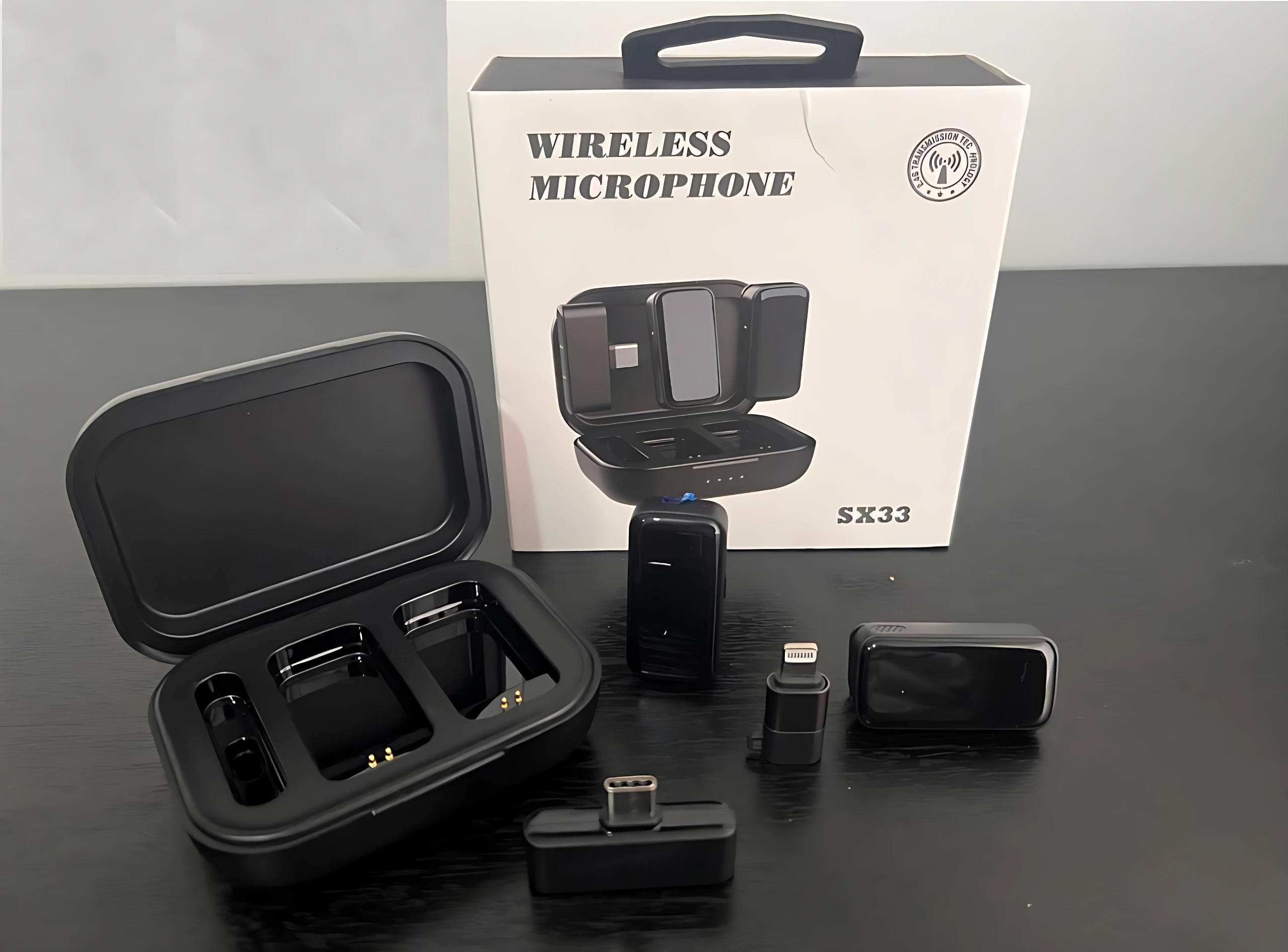 Caja abierta de micrófono inalámbrico modelo SX33 con accesorios, incluyendo receptor, micrófono y cargador, sobre superficie oscura.