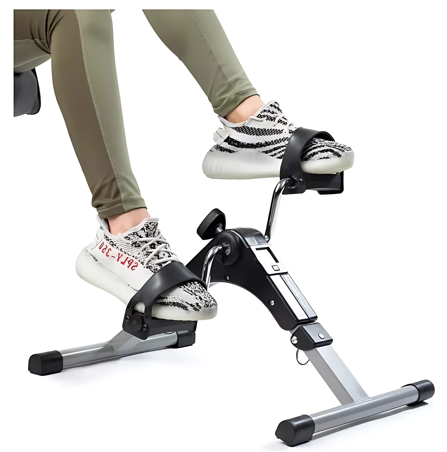Mini bicicleta spinning compacta en uso, con usuario usando zapatillas blancas y leggings verdes, mostrando pedales ajustables y estructura metálica gris y negra.
