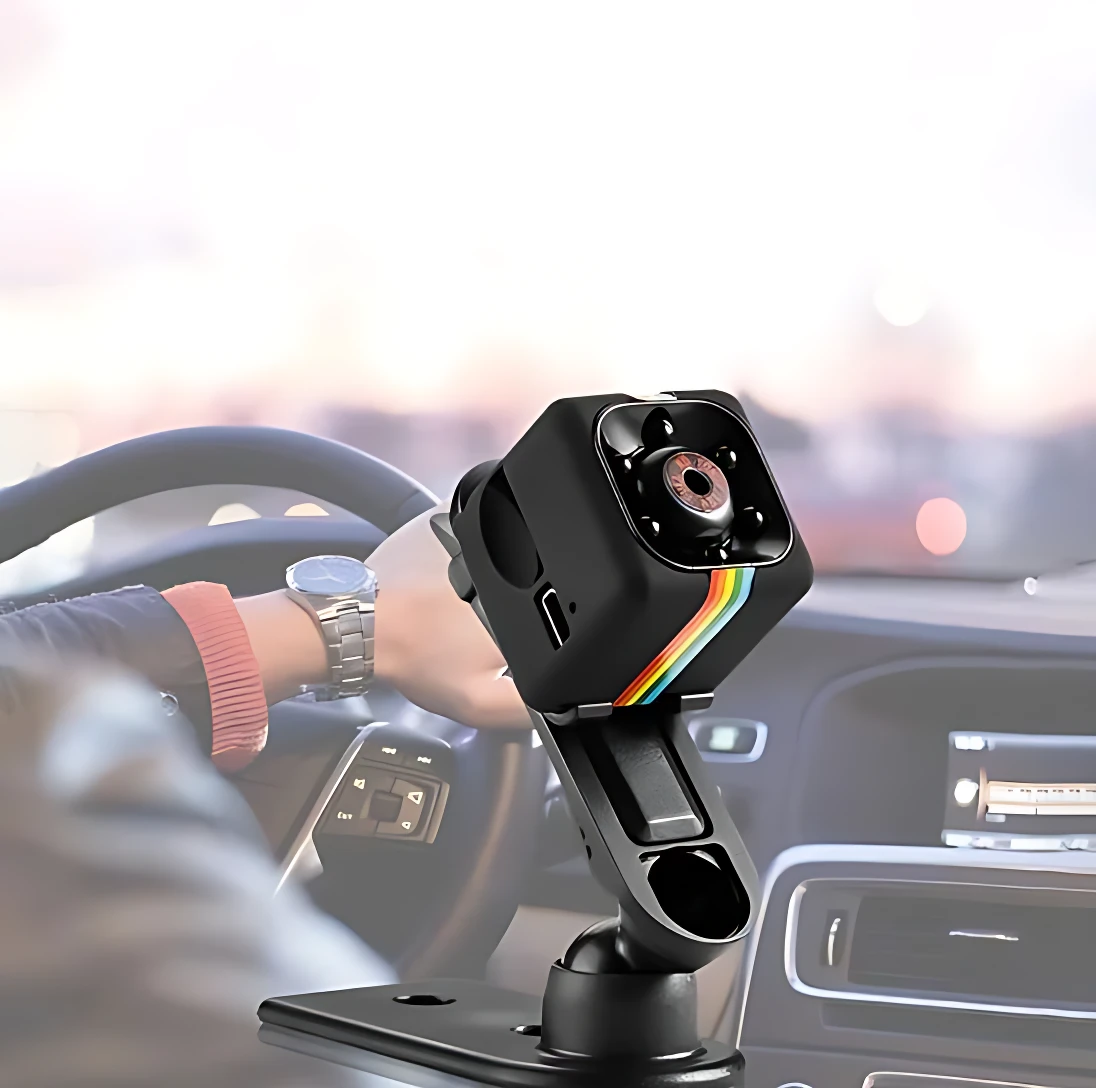 Cámara de seguridad espía negra con lente frontal y detalles multicolores, montada en soporte ajustable sobre salpicadero de automóvil.