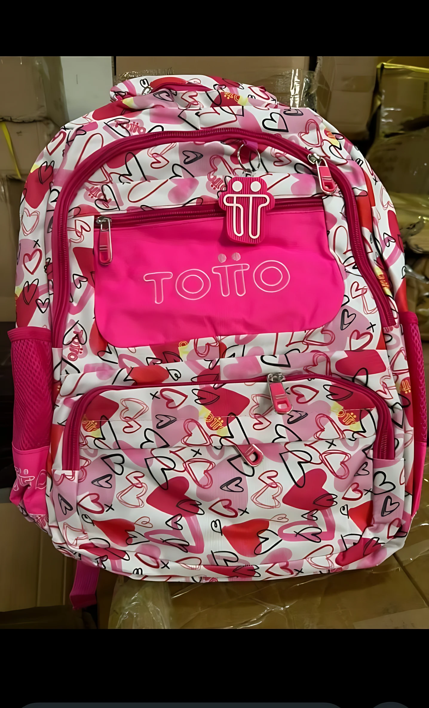 Mochila escolar juvenil tipo Totto en estampado geométrico rosa y blanco, con compartimentos frontales y laterales para distribución de peso.
