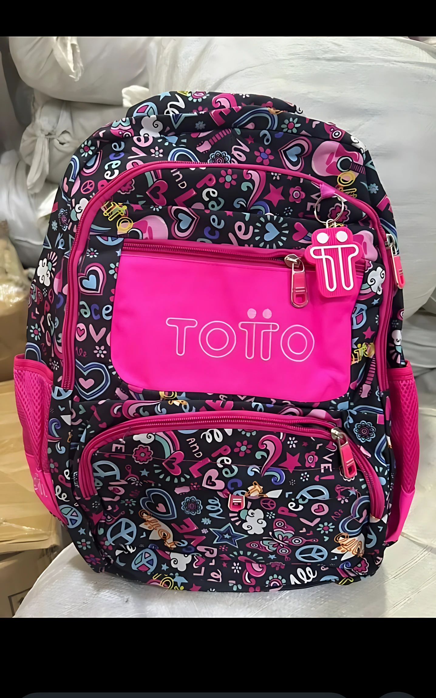 Mochila escolar juvenil tipo Totto con diseño geométrico multicolor, panel frontal rosa brillante y detalles en tonos neón.