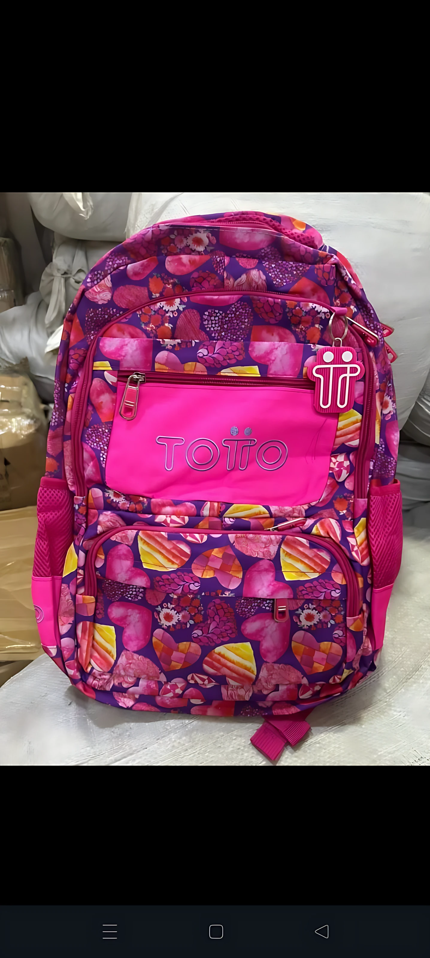 Mochila escolar juvenil tipo Totto en tonos magenta y fucsia, con estampado geométrico de corazones y formas abstractas, compartimentos frontales visibles y asas ergonómicas.