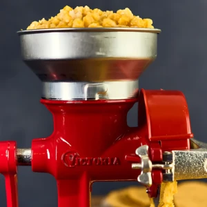Molino de granos en hierro fundido color rojo con tolva metálica llena de maíz amarillo, mostrando salida de producto procesado.
