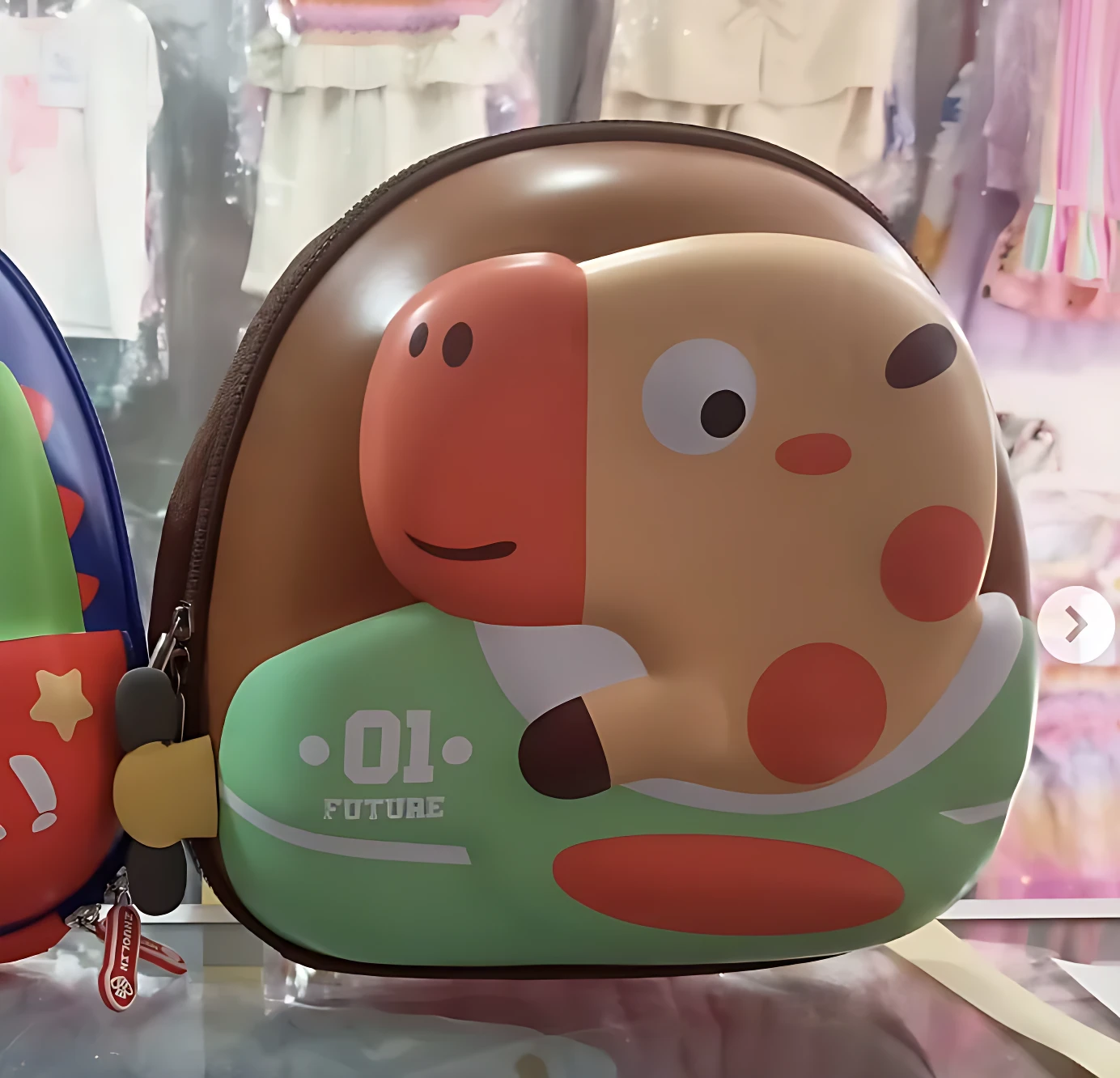 Mochila infantil rígida de color marrón con diseño tridimensional de jirafa en tonos naranjas y verdes, mostrando el frente con detalles gráficos y cierre lateral visible.
