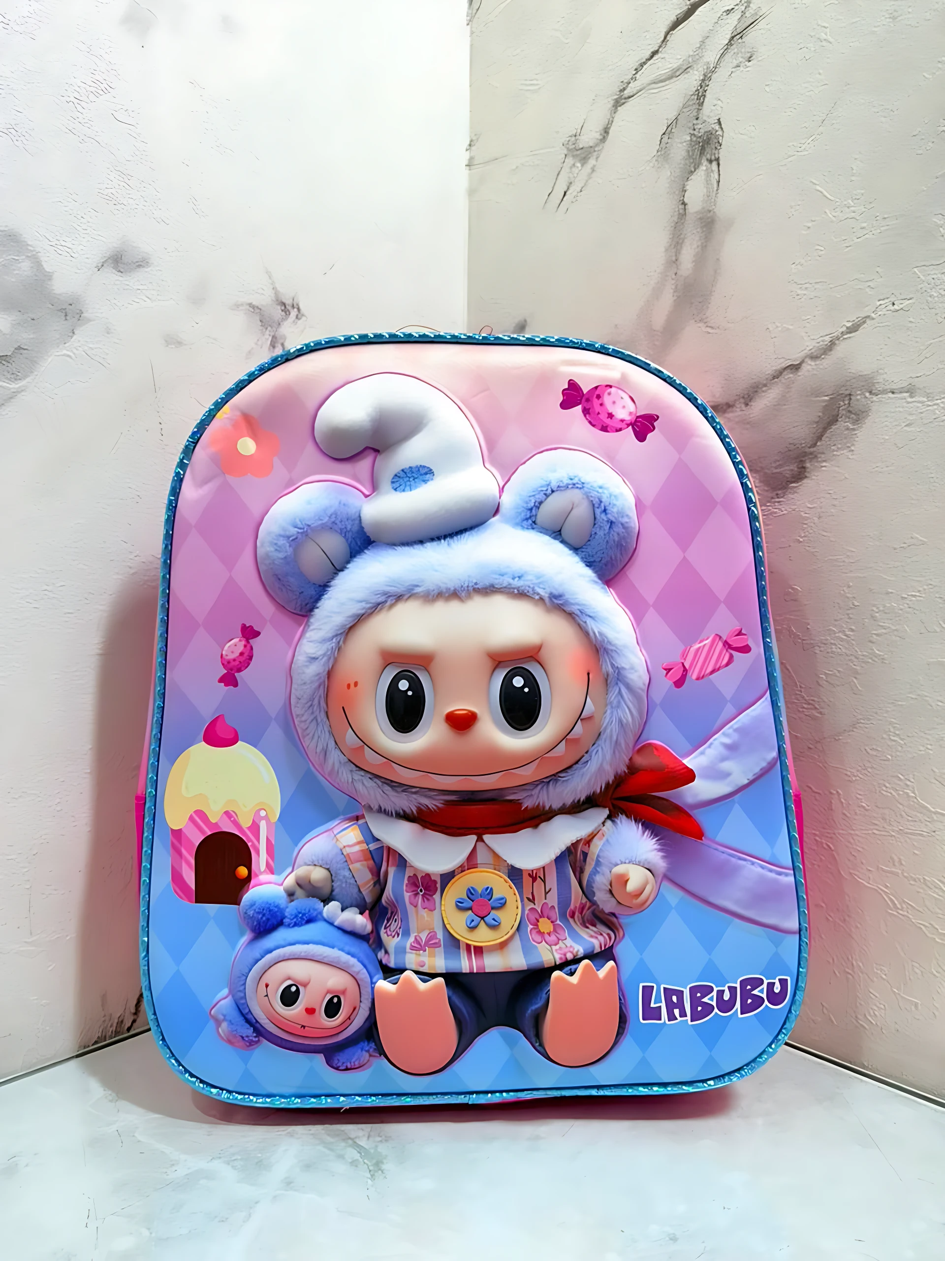 Mochila escolar infantil compacta con cierre único, diseño 3D de personaje LREUBU en tonos rosa y azul, con detalles de peluche y accesorios visibles.