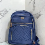 Morral Origen Mn64 en azul marino con costura entrelazada y cremalleras doradas, acompañado de llavero de monedita.
