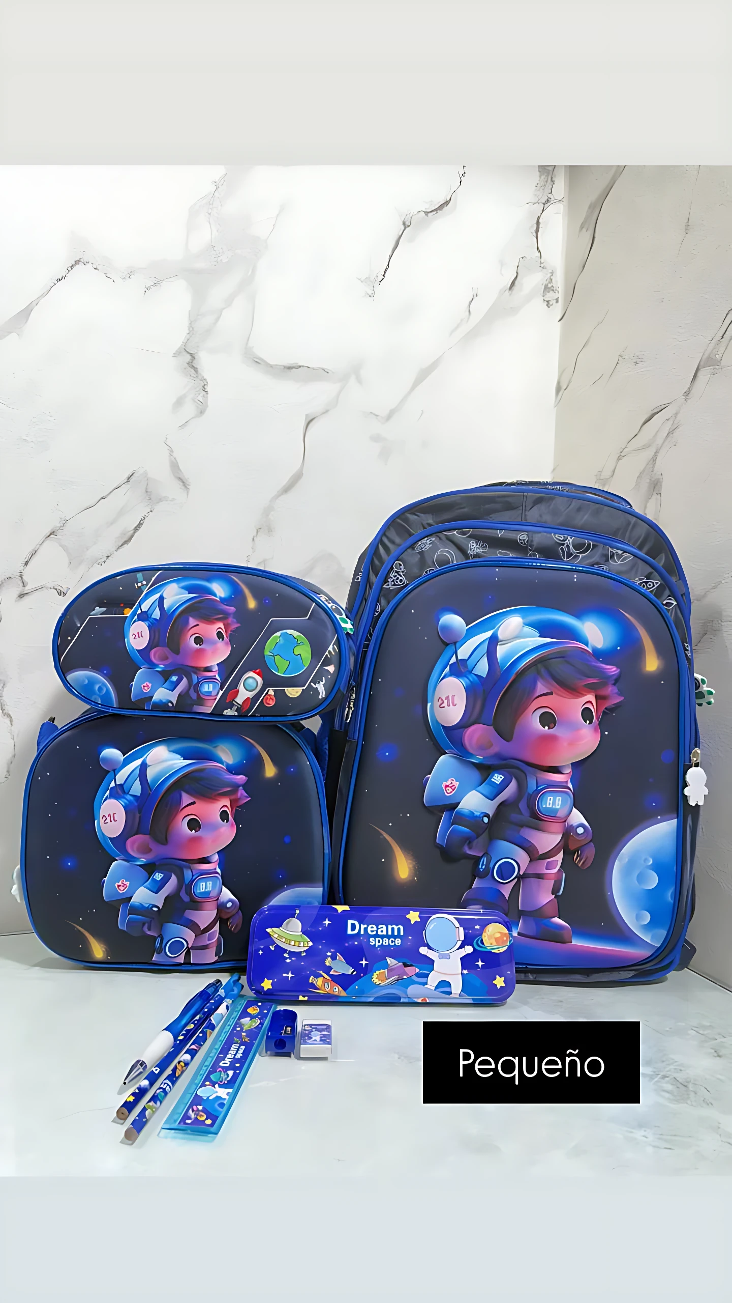 Mochila escolar pequeña azul con diseño espacial de astronauta, incluye lonchera integrada y estuche con lápices y bolígrafos.