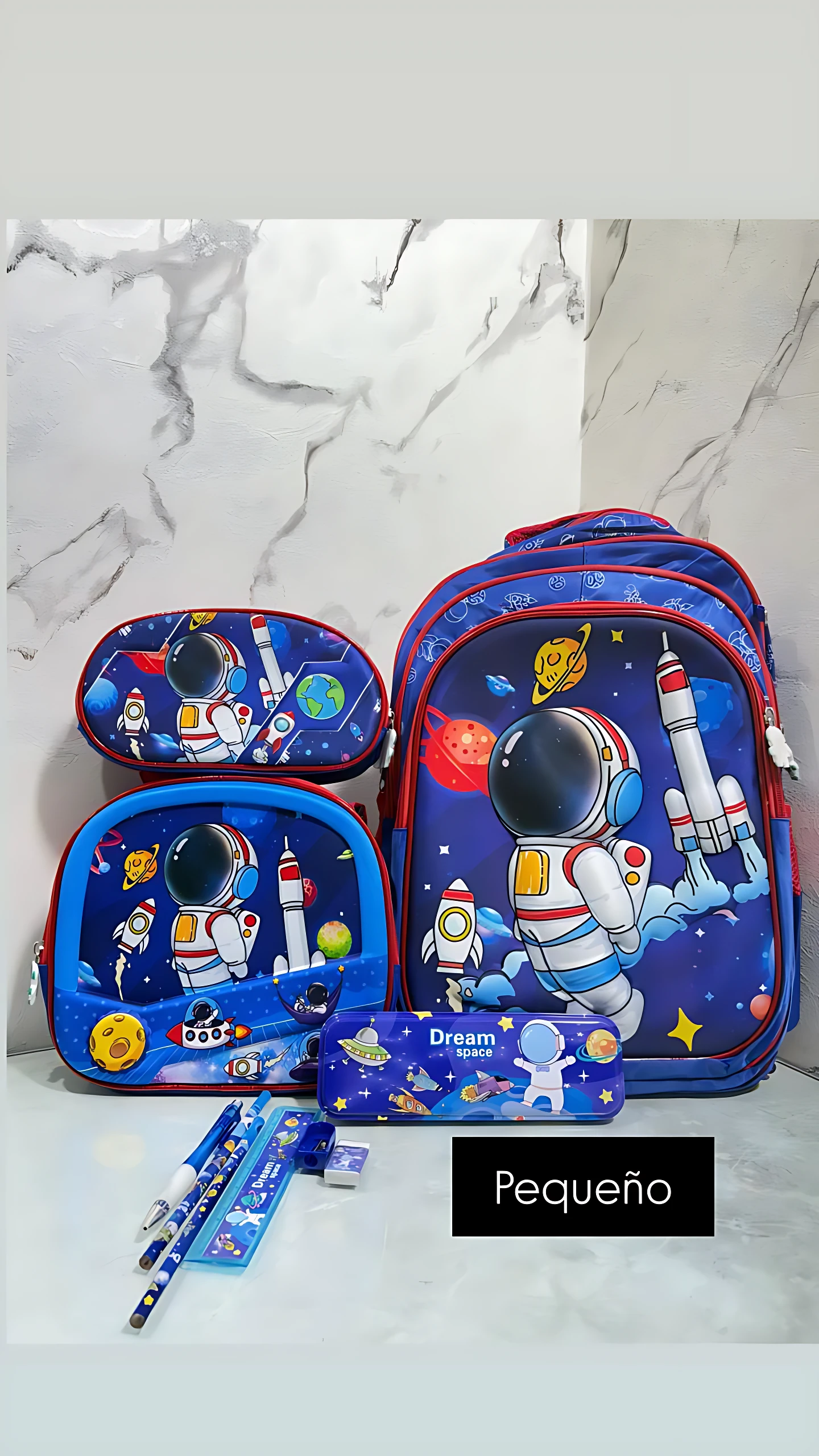 Mochila escolar pequeña azul con temática espacial, incluye lonchera integrada, estuche y accesorios. Etiqueta indica variante Pequeño.