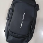 Morral rígido antirrobo negro con combinación, vista superior mostrando asa lateral y logo "FASHION" en frontal.